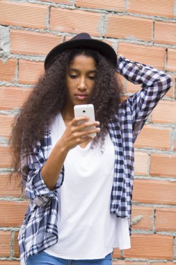 Şapkalı Afro kız cep telefonuna bakıyor