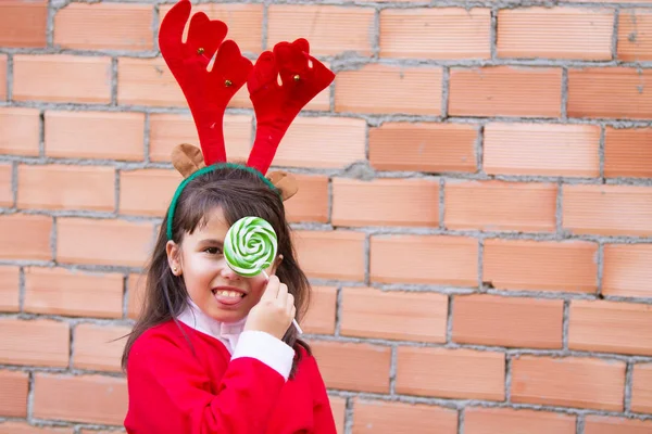 Little pretty girl with reindeer antlers hat and colorful lollipops