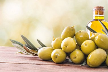 Arka planda zeytin ve bir şişe ekstra saf yağ var.
