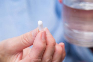 Elinde haplar, kapsüller ve bir bardak su olan bir kadın.