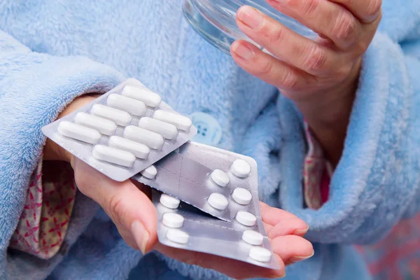 woman with pills or capsules on hand and a glass of water