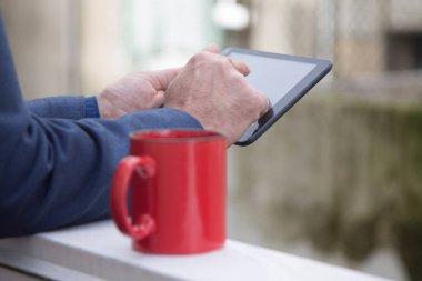 Tablet ya da e-kitap kullanan bir adam bir fincan kahvenin yanında.