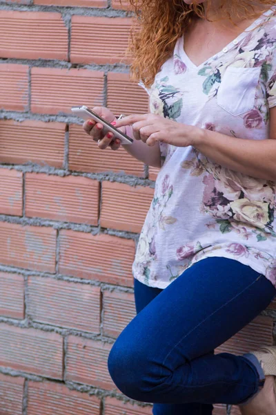 レンガの壁にもたれている携帯電話を持つ赤毛の女性 — ストック写真