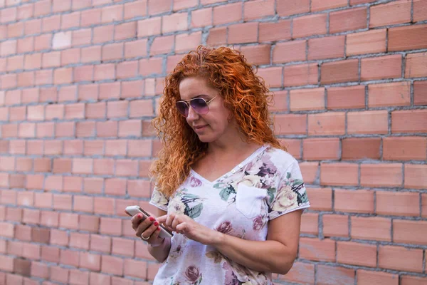 レンガ壁の背景を持つ携帯電話を使う女性は — ストック写真