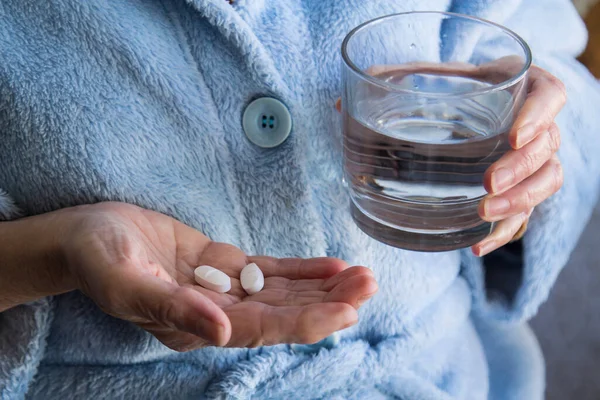 woman with pills or capsules on hand and a glass of water