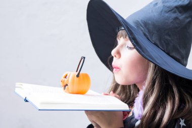 Kitap büyüleri ve balkabağı ile cadı gibi giyinmiş bir kız. Cadılar bayramı partisi