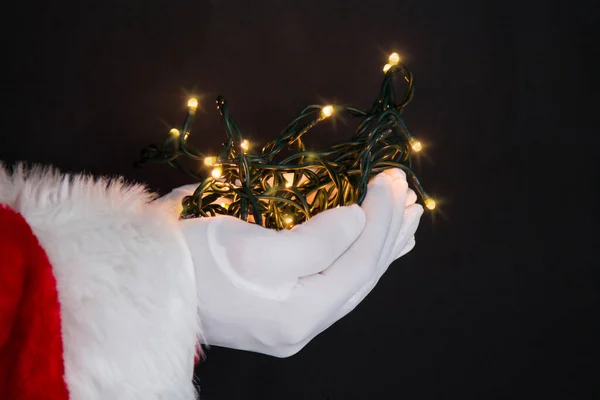 サンタクロースの手は背景にクリスマスライトを保持 — ストック写真
