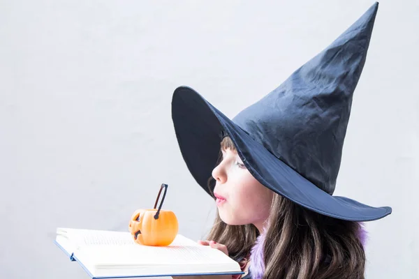 girl dressed as a witch with book spells and pumpkin. halloween party
