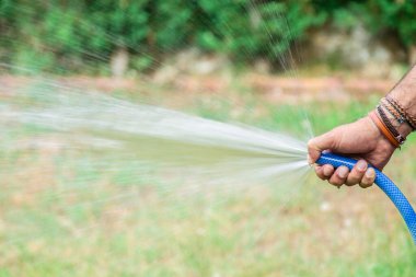 Çimleri hortumla sulayan adam.