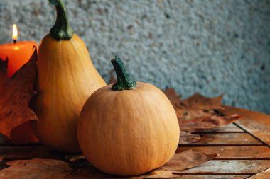 Balkabağı, kurumuş yapraklar ve ahşap bir masada mumlarla dekoratif bir hayat.