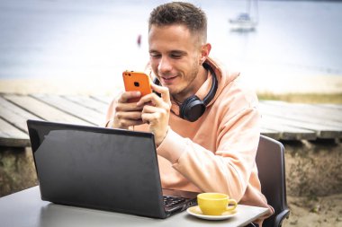 Kahve dükkanının terasında oturan genç bir adam yeni teknolojiyle çalışıyor.