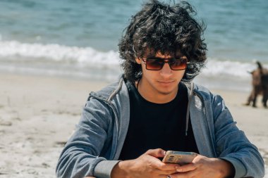 Genç ve çekici bir adam plajda güneş gözlüğü takıyor.