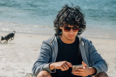 Genç ve çekici bir adam plajda güneş gözlüğü takıyor.