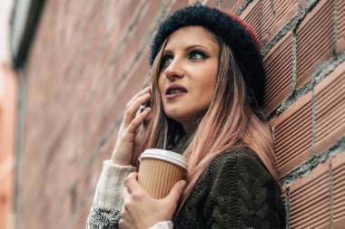 Tuğla duvara yaslanmış, telefonu olan ve paket servisi yapan rahat genç bir kadın.