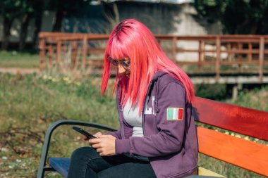 Gökkuşağı renginde bankta otururken cep telefonunu kullanan güzel bir kadın..