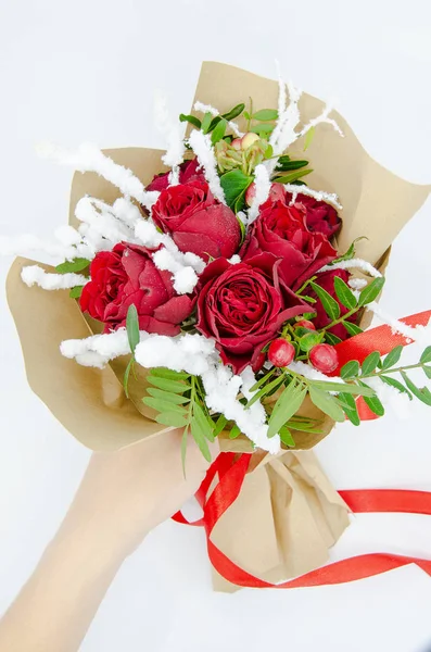 Beyaz bir arka plan üzerinde izole kahverengi kağıt ile kış yeşil kırmızı gül buketi tutan el sarılı