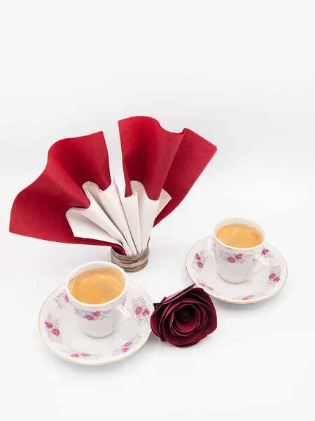 İki çiçek süslü porselen fincan espresso kahve ve bir yuvarlak peçete halkası tutucu bir kağıt peçete kırmızı kağıt gül, beyaz bir arka plan üzerinde izole studio ile dekore edilmiş
