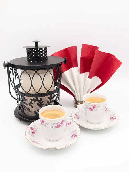 İki çiçek porselen fincan espresso kahve siyah metal mum fener ve beyaz bir arka plan üzerinde izole bir peçete halkası tutucu bir kağıt peçete ile süslü
