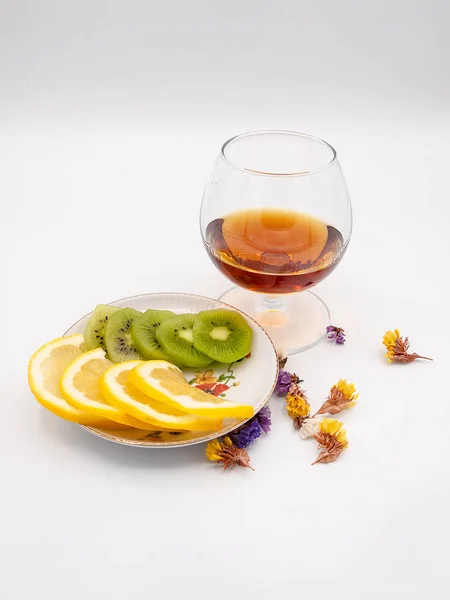 Beyaz bir arka plan üzerinde izole limonium çiçek bardak viski veya konyak bir tabak dilimlenmiş limon ve kivi ile süslenmiş