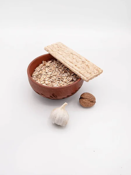 Beyaz bir arka plan üzerinde seramik tabak bir diyet gevrek ekmek veya bir sarımsak ve ceviz, sağlıklı beslenme, bir kavram olarak dekore edilmiş bisküvi ile kuru yulaf ezmesi izole