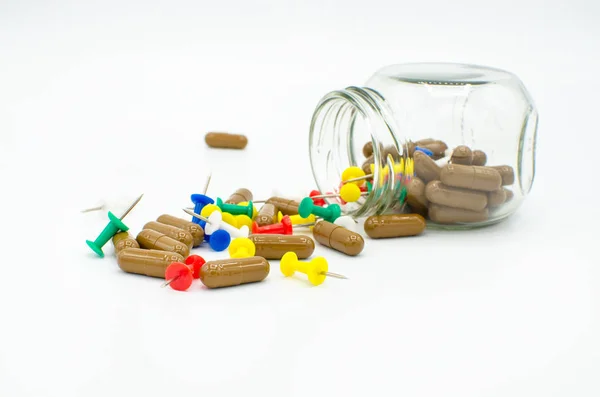 Renkli itme bağlantıları veya beyaz bir arka plan üzerinde ağrı, hastalık, tıbbi ya da aşırı dozda ilaç bir kavram olarak izole çiviler ile karışık dağınık kahverengi kapsül haplarla üzerinde cam eğik