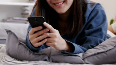 Çinli kız yatakta yatarken akıllı telefon kullanıyor.