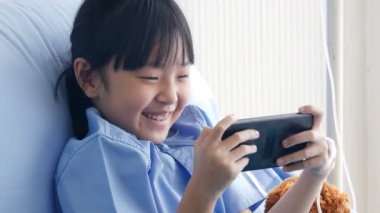 Asyalı küçük kız hastane yatağında oyun oynuyor