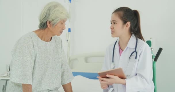 診療所の先輩患者さんと話す女性医師 医師はタブレットを使用して病院で高齢女性と情報を見つけ 話をする — ストック動画