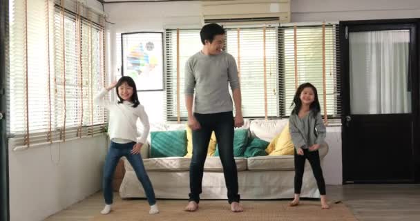 若い父親と女の子の音楽を聞いて一緒にジャンプダンス 彼らは現代のリビングルームで一緒に家でレジャーライフスタイルを楽しんでいます — ストック動画