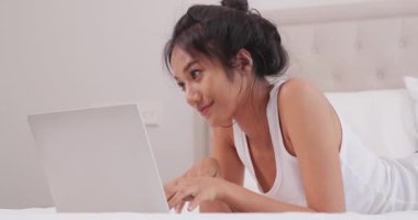 Yatakta yatarken dizüstü bilgisayar kullanan güzel Asyalı kadın.