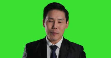 Asyalı takım elbiseli adam yeşil arka planda poz veriyor.