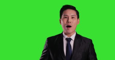 Asyalı takım elbiseli adam yeşil arka planda poz veriyor.