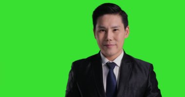 Asyalı takım elbiseli adam yeşil arka planda poz veriyor.