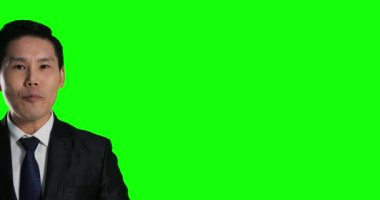 Asyalı takım elbiseli adam yeşil arka planda poz veriyor.