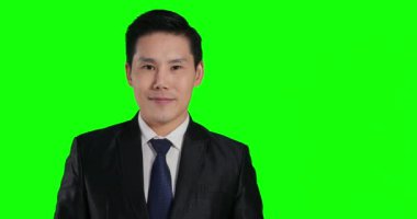 Asyalı takım elbiseli adam yeşil arka planda poz veriyor.