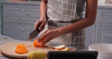 Güzel bir kadın şık bir mutfakta yemek pişiriyor ve tablet bilgisayar kullanıyor.