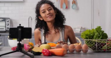 Güzel bir kadın şık bir mutfakta yemek pişiriyor ve akıllı telefon kullanıyor.