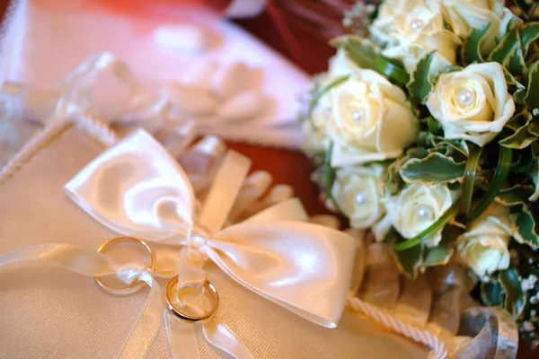 Close up of wedding rings of the newlyweds with the flowers bouquet in the background — Stock Photo, Image