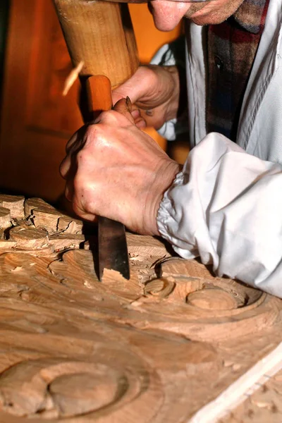 Craftsman carves wood with chisel.