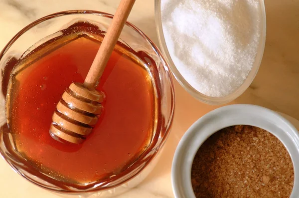 Κοντινό σε επίπεδη γωνία ενός δοχείου μελιού δίπλα στη λευκή ζάχαρη και τα κύπελλα καφέ ζάχαρης. — Φωτογραφία Αρχείου