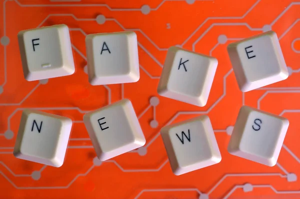 Tasti della tastiera formano la parola FAKE NEWS sul circuito elettrico arancione sullo sfondo . — Foto Stock