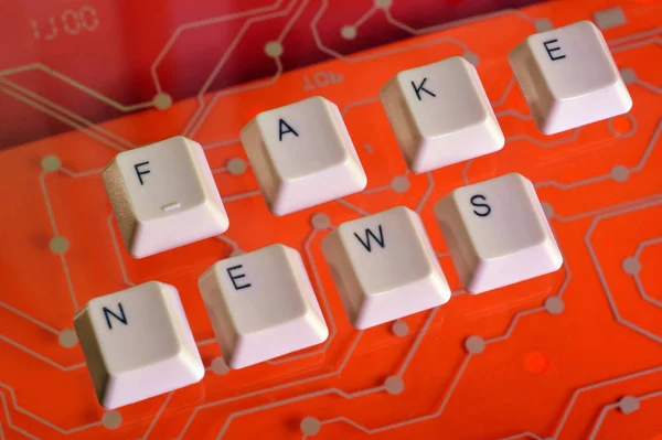 Tasti della tastiera formano la parola FAKE NEWS sul circuito elettrico rosso sullo sfondo . — Foto Stock