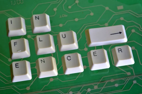 Клавиатурные клавиши образуют слово INFLUENCER на зеленой электрической цепи в фоновом режиме — стоковое фото