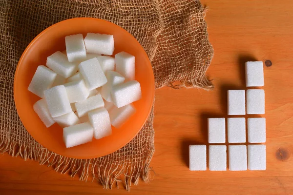 Bol à sucre orange rempli de cubes de sucre sur une table en bois avec une composition graphique . — Photo