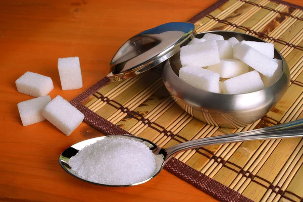 Un bol plein de cubes de sucre et une cuillère pleine de sucre blanc raffiné sur une table en bois . — Photo