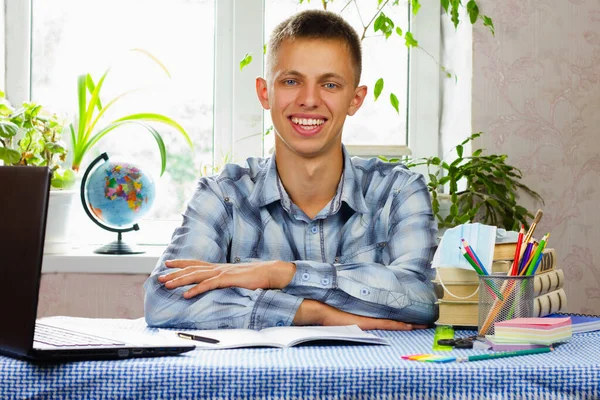 The young man sits at the workplace and smiles against the background of the room.