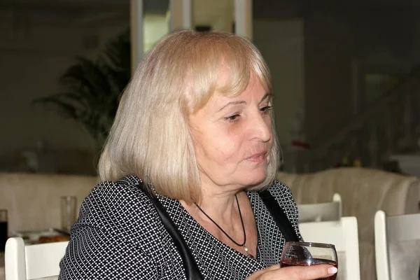 Atraktivní elegantní blondýnka starší žena s bob účes drží sklenku červeného vína na přípitek, sedí u stolu. — Stock fotografie