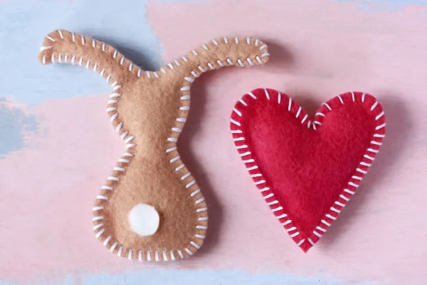 Beige Kaninchen und rotes Herz auf blassrosa Hintergrund. Valentinstag oder frohe Ostern Hintergrund für Grußkarte Vorlage. Handgefertigt aus Filz. , — Stockfoto