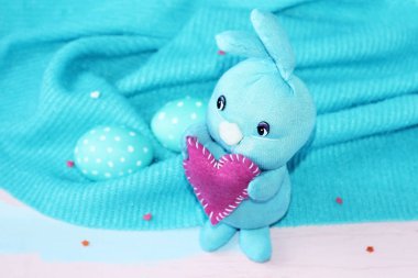 Mavi ve beyaz lekelenmiş yumurta ile mavi bir arka planda onun pençeleri bir kalp ile Paskalya mavisi tavşan. El yapımı. Happy Easter için tebrik kartı arka planı.