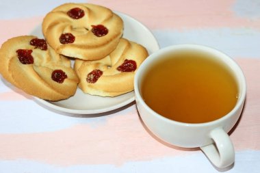 Kiraz reçel ve pembe-açık mavi ahşap masada yeşil çay bir kupa ile kısa ekmek çerezleri.